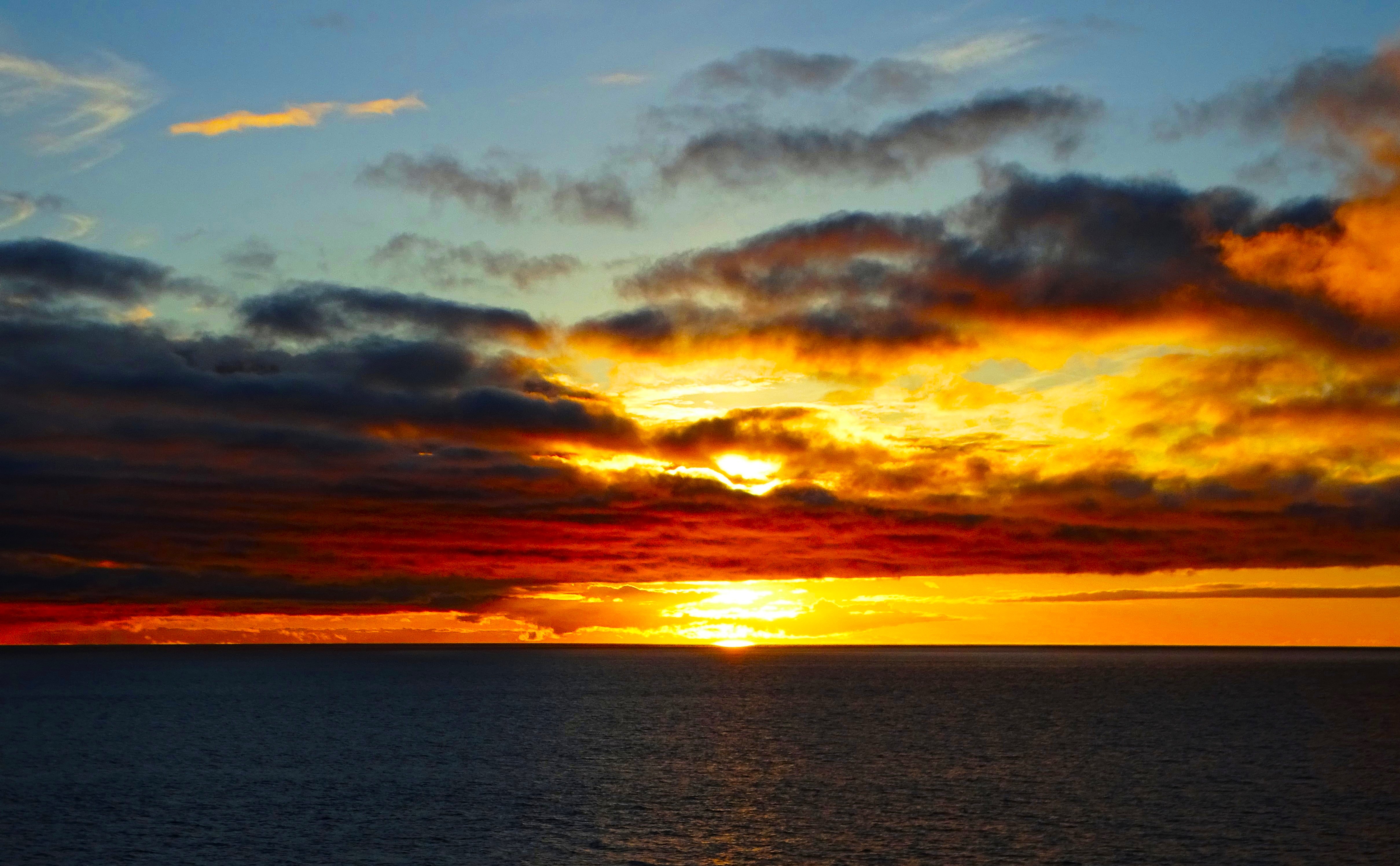 A vibrant sunset over the ocean, with dramatic clouds in shades of orange, red, and blue.