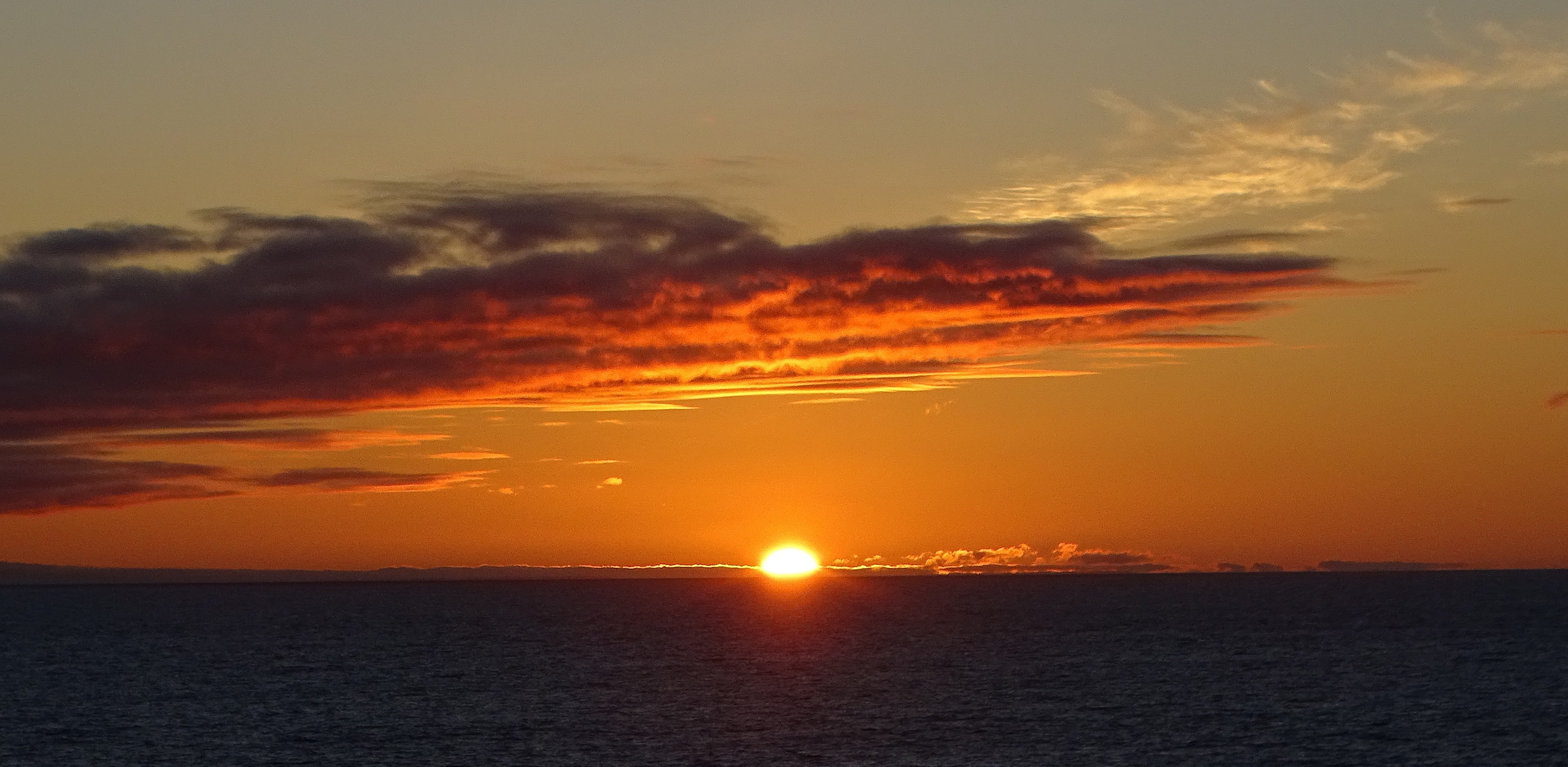 A vibrant sunset over the ocean, with bright orange and red hues illuminating the sky and reflecting on the water.