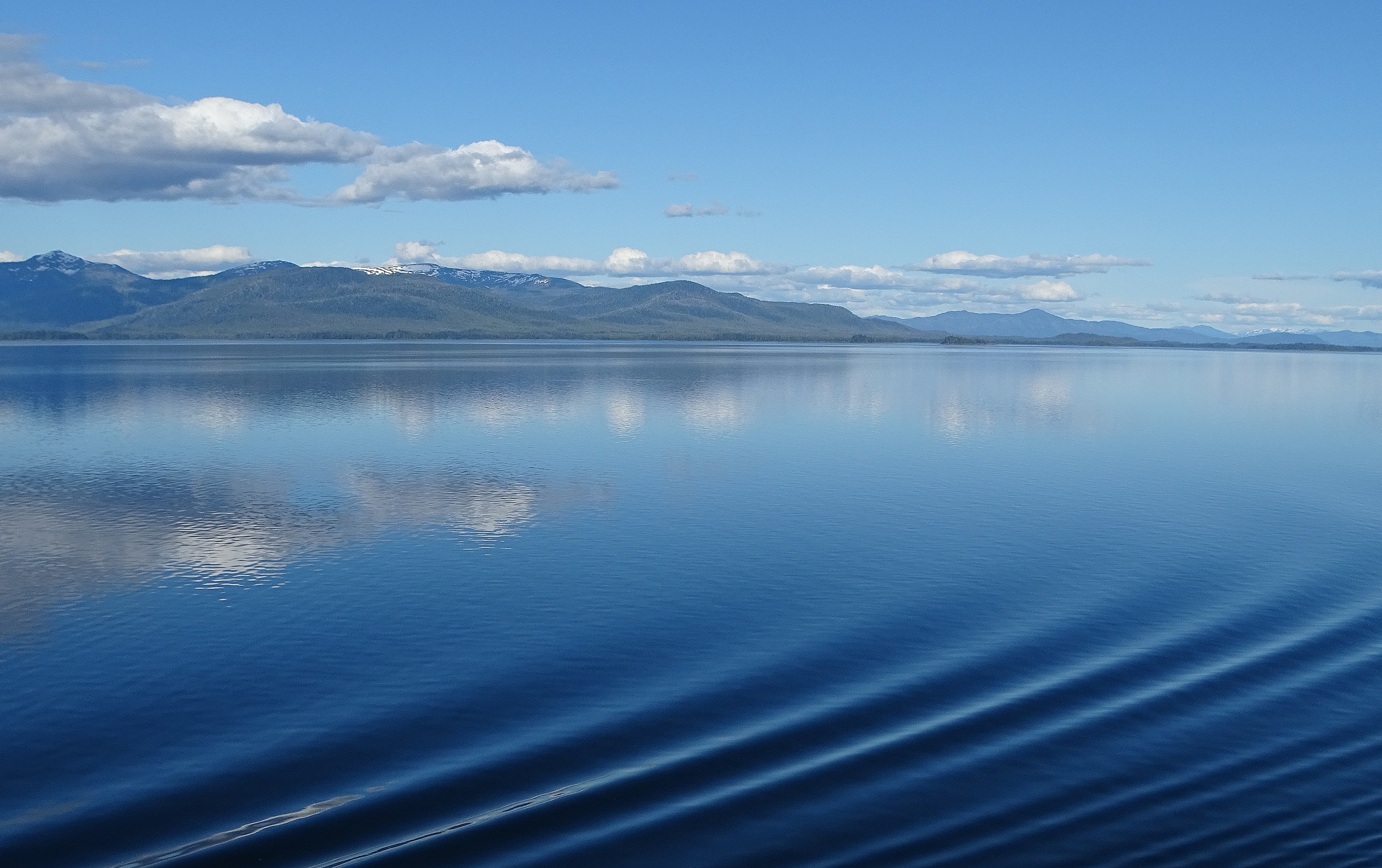 A serene lake reflecting the blue sky and clouds, with distant mountains in the background.